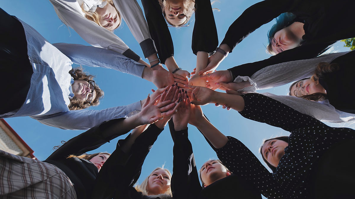 Students joining hands together in a circle, symbolizing unity and teamwork on a bright school day